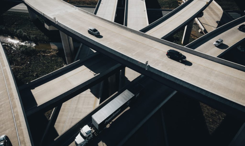 multi-tiered freeway with cars passing and one large white truck on the lower level 