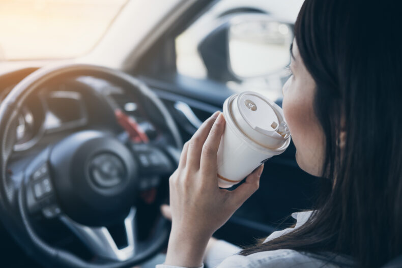 woman holding white coffee cup drinking while distracted driving