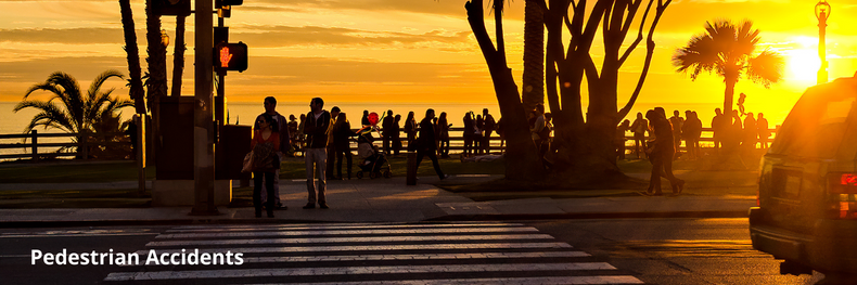 two pedestrians waiting at a crosswalk to cross the street at sunset with a crowd of people in the background observing the ocean and the sun setting