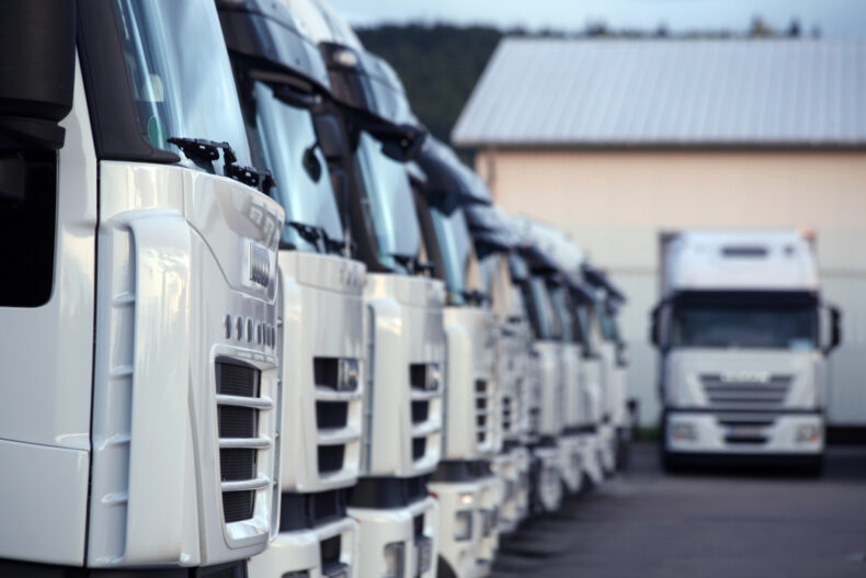 close up perspective of lined up white trucks that are driven by a semi-truck driver 